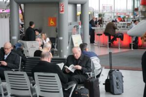 Joachim Kardinal Meisner mit Altpapier in der Abflughalle des Kölner Adenauer-Airports - auf dem Weg in die Homo-Hölle? Man weiß es nicht. (Foto: Bundesamt für magische Wesen)